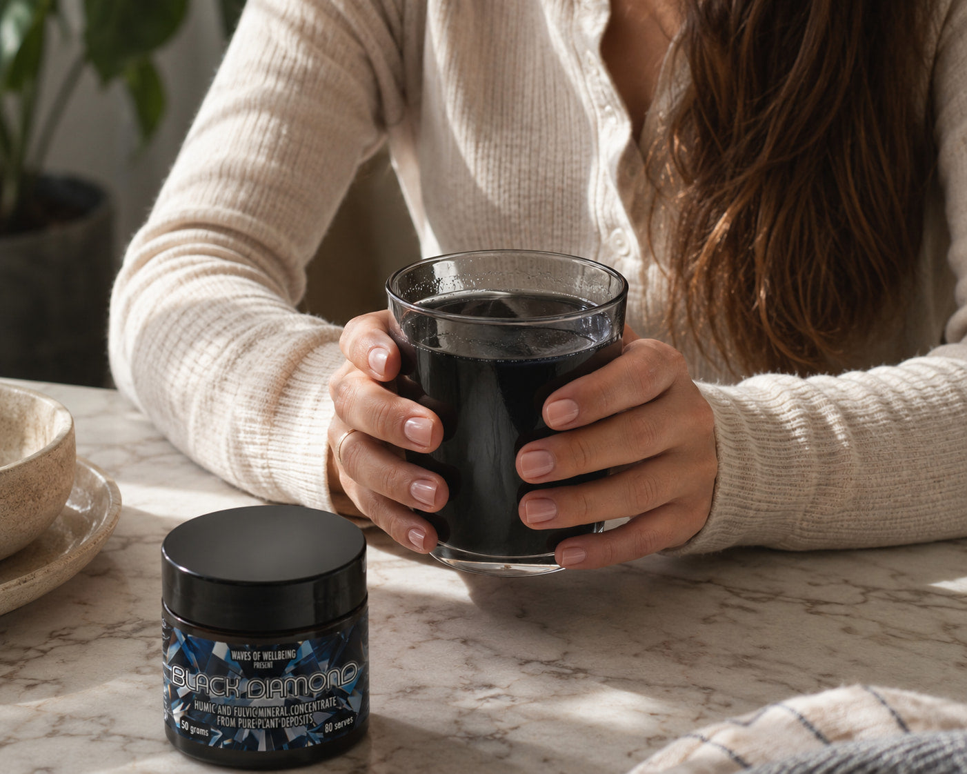 Woman holding a glass of mineral-infused drink beside Black Diamond jar