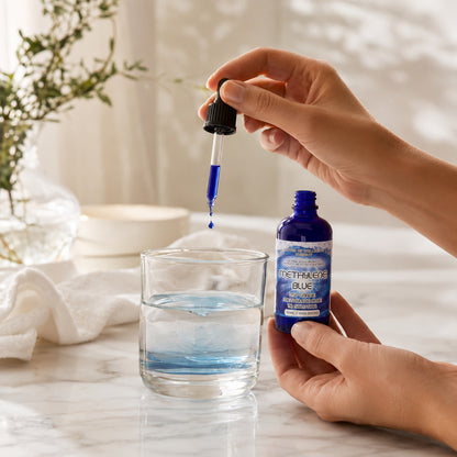 Hand holding a bottle of Methaqua Blue and dropping it into a glass of water on a marble surface.