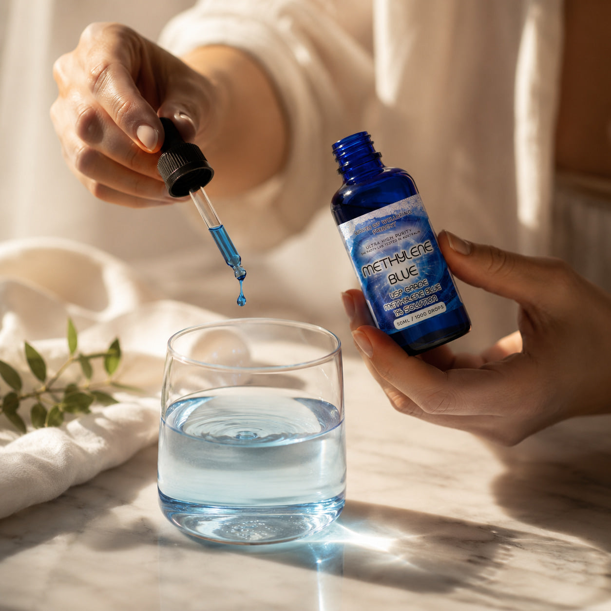 Waves of Wellbeing methylene blue 50ml USP grade being added to a glass of water - morning wellness ritual with blue drop falling from dropper